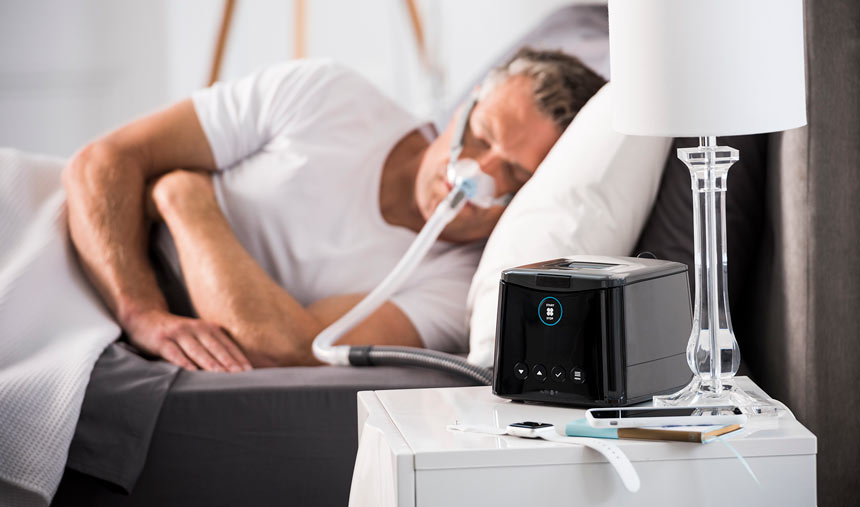 一位患者佩戴着 Eson2 睡眠呼吸暂停鼻罩睡觉，床头桌上放置着配套的费雪派克 (F&P) Sleepstyle 呼吸机。